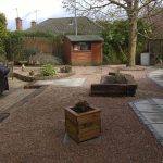 wooden plant pot in gravel stones alongside concrete pavement